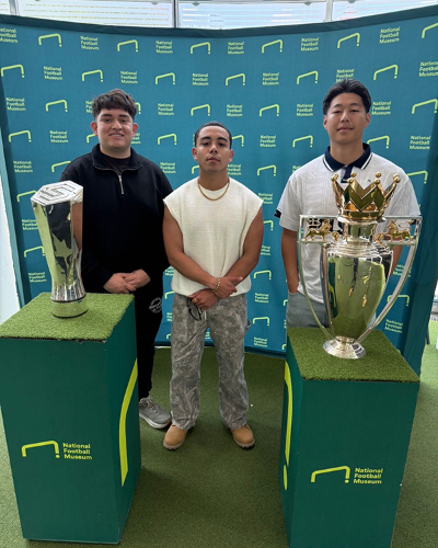 LSU management major Joseph Perez join other students in visiting the National Football Museum in Manchester, England. They stand in front of a branded backdrop and pose with trophies.